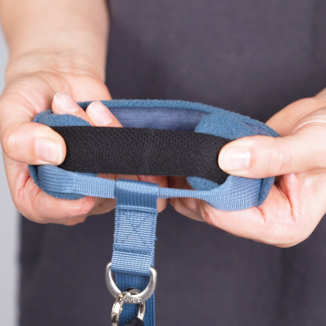 Close-up of hands fastening a blue adjustable strap with a black hook-and-loop closure and metal ring