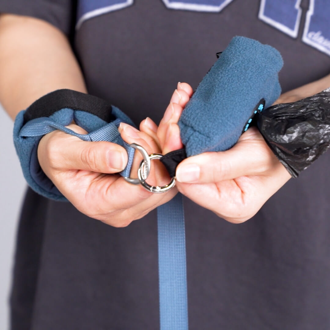 Close-up of hands fastening a blue leash clasp and padded handle