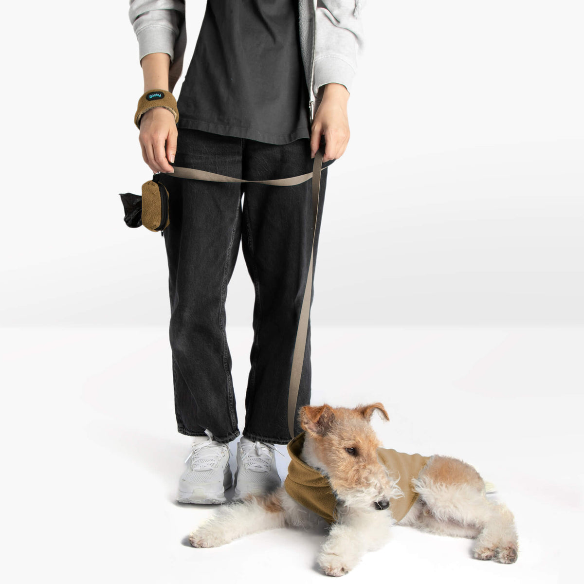 Dog wearing a beige zip-up fleece vest with a matching leash beside a person