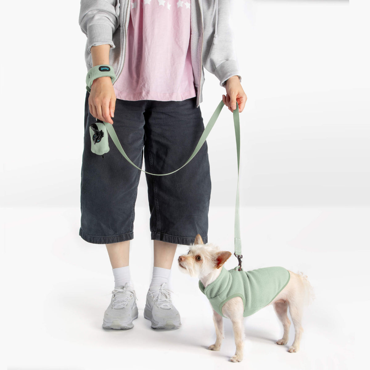 Dog wearing a mint fleece vest with a matching leash beside a person