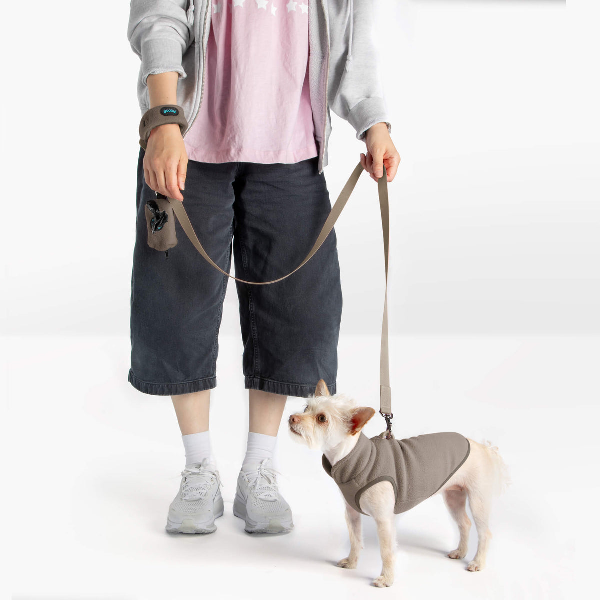 Dog wearing a warm gray fleece vest with a matching leash beside a person