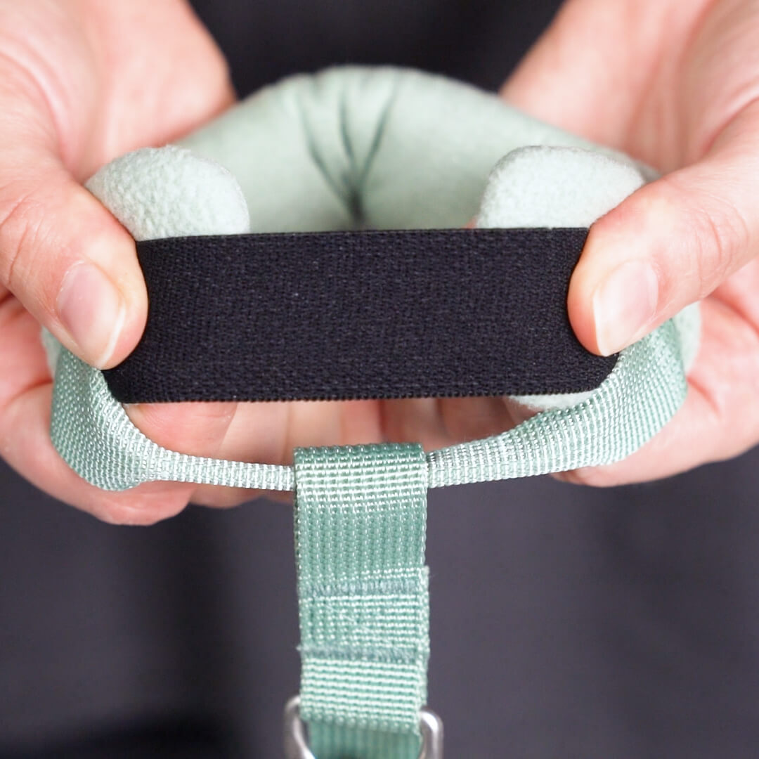 Close-up of hands adjusting the black fastening strap on a pale green leash