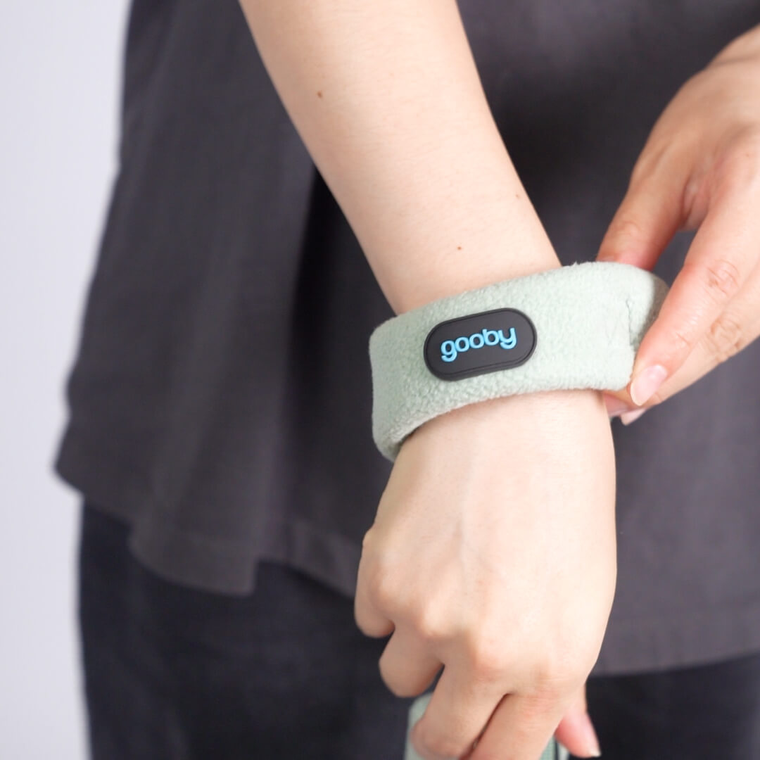 Close-up of a person fastening a soft mint-green strap with a gooby logo around their wrist