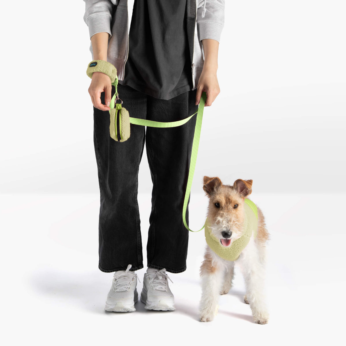 Dog wearing an avocado sherpa puffer vest with matching leash beside a person