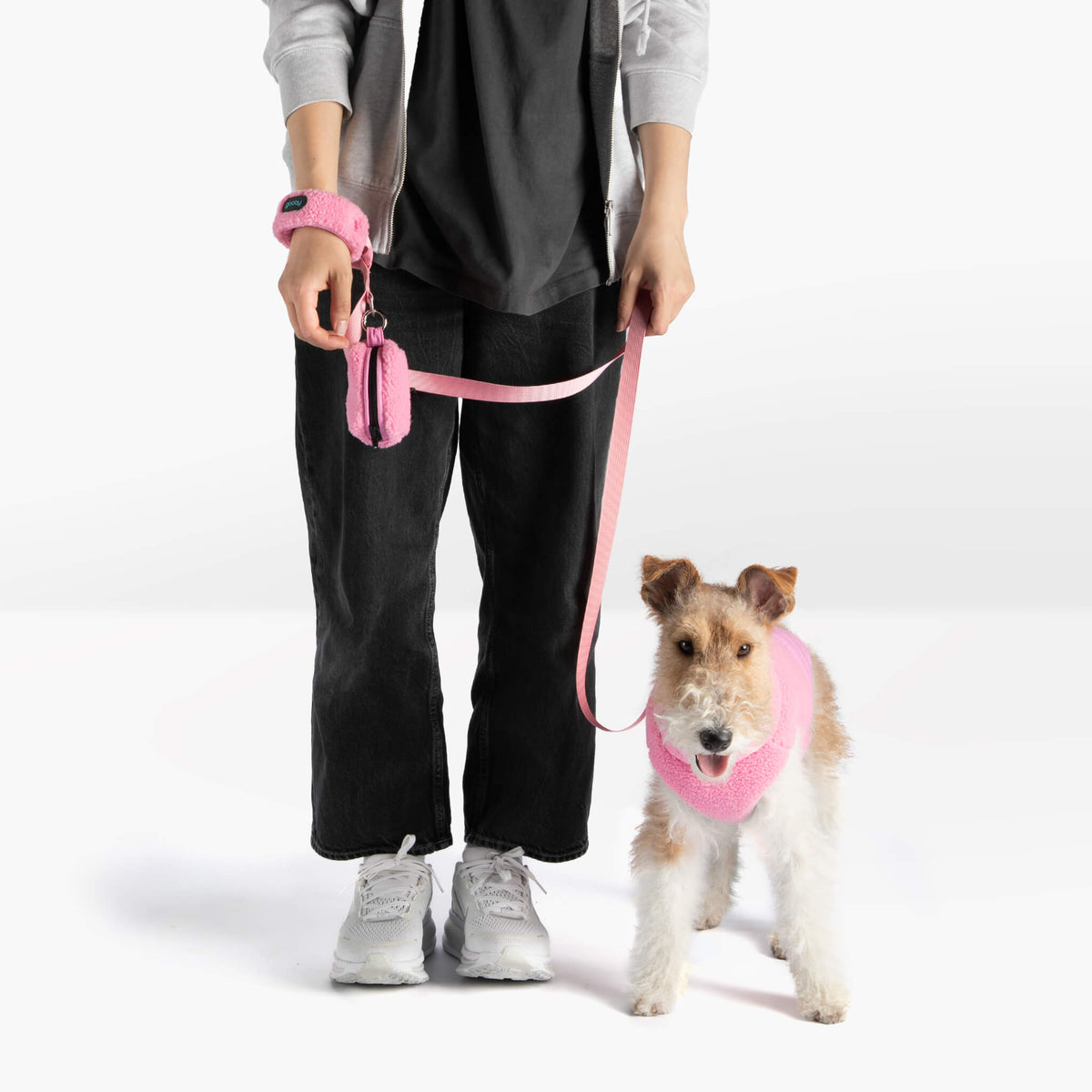 Dog wearing a baby pink sherpa vest and matching leash beside a person