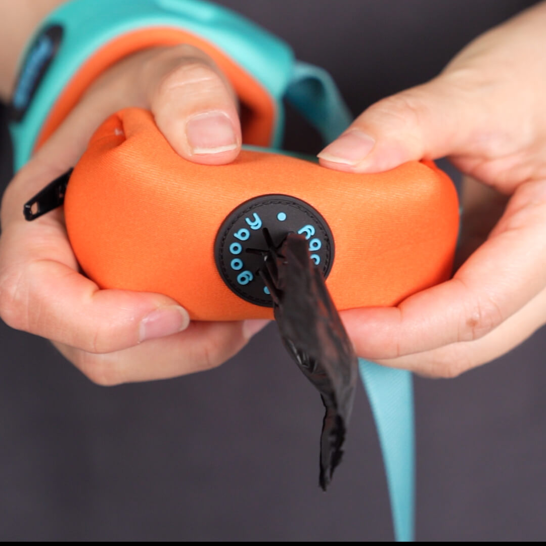Close-up of hands adjusting an orange leash attachment with a black rotating dial and turquoise strap behind it.