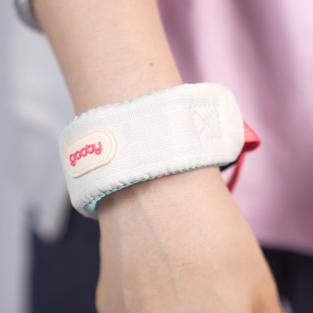 Close-up of a white wrist strap with a pink logo worn around a person's wrist