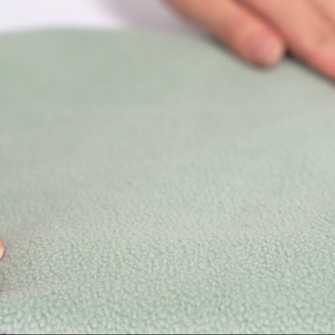 Close-up of soft mint-green fleece fabric with a hand touching the textured surface