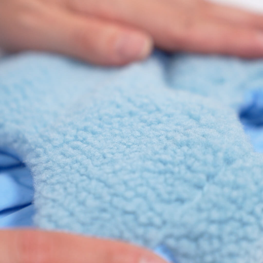 Close-up of soft light blue sherpa fleece fabric held between fingers
