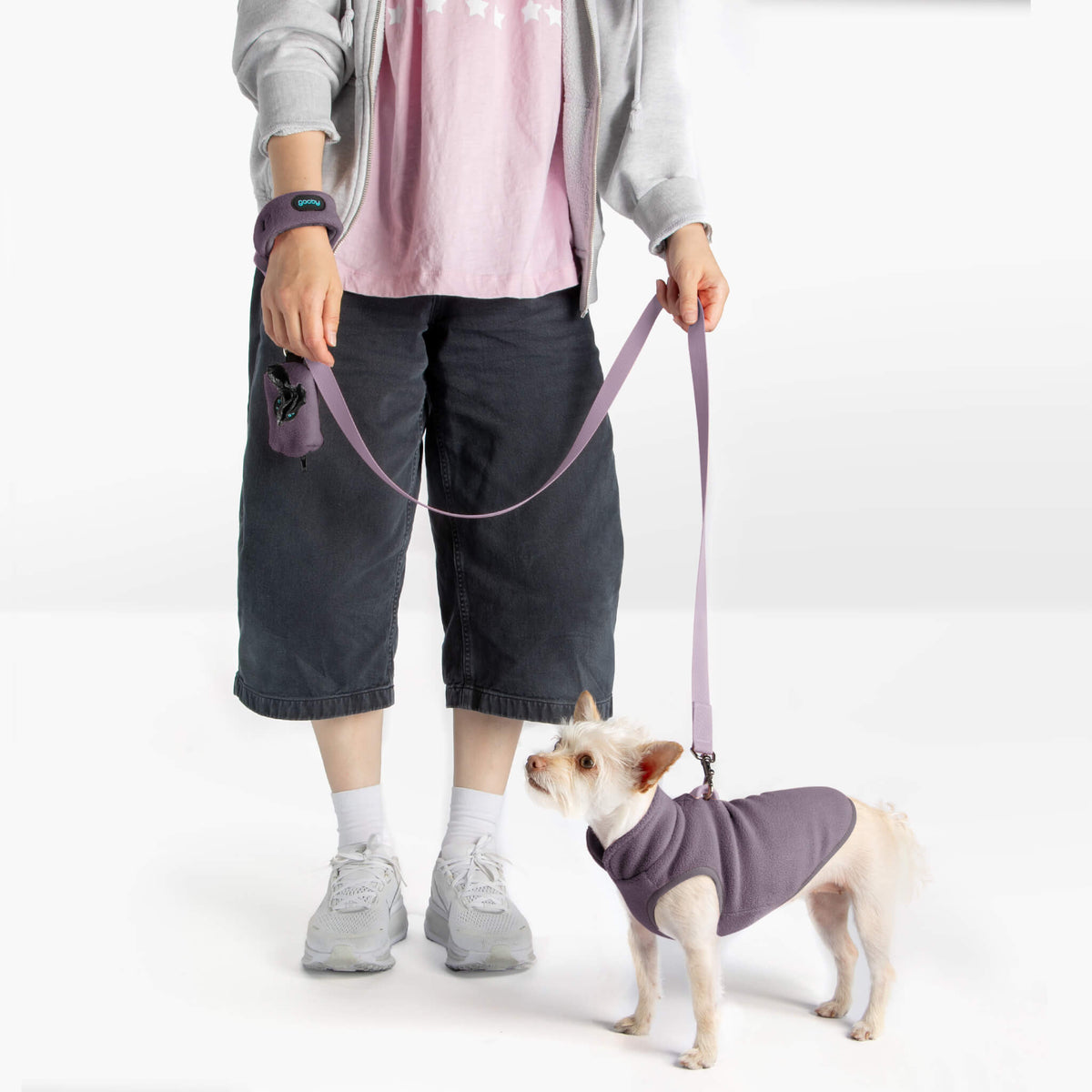 Person wearing a lavender fleece matching set with a small dog in a matching vest and leash