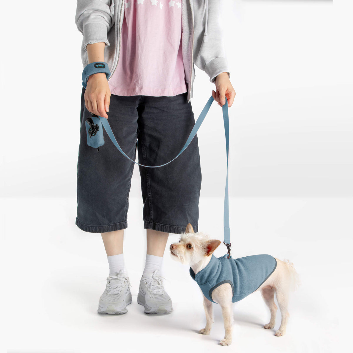 Dog wearing a steel blue fleece vest and matching leash beside a person