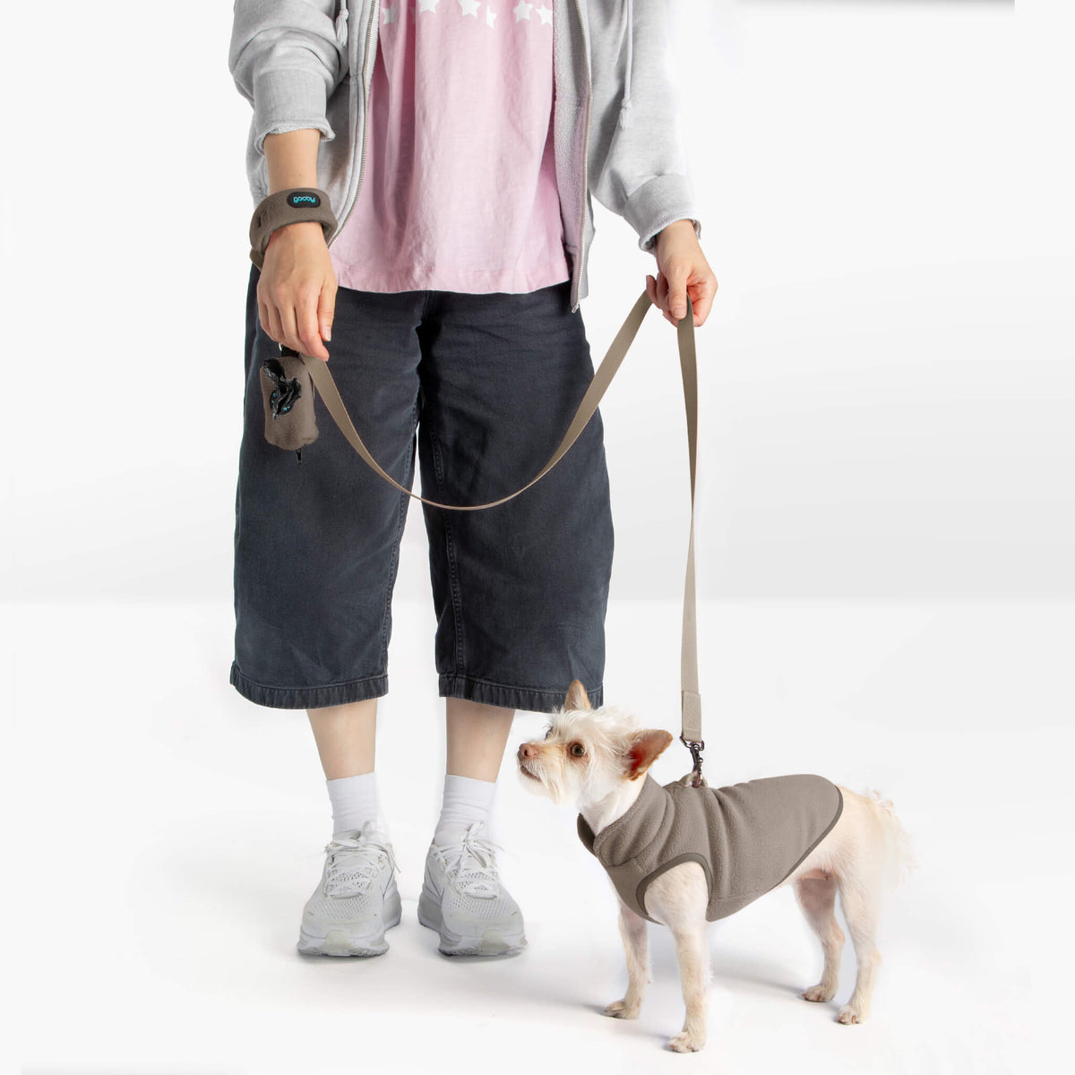 Dog wearing a warm gray fleece vest on a matching leash beside a person