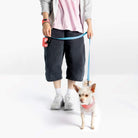 Person walking a small dog wearing a pink harness with a blue leash