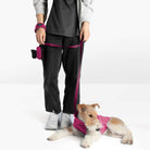 Person holding a magenta dog leash while a terrier wearing a matching magenta vest lies on the floor